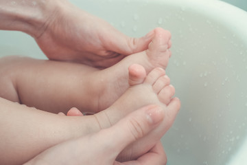 mother holding and massage baby's feet while taking a bath in bathtub. vintage photo and film style.