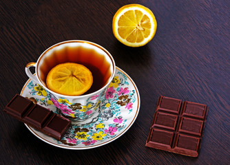 Strong rich hot black tea with a slice of lemon and a piece of chocolate on a saucer.