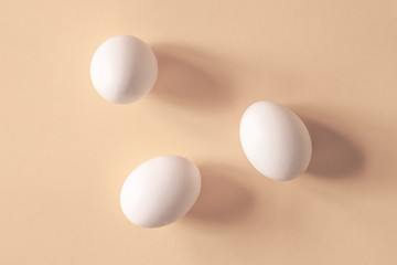 Minimalistic composition of three white crepe eggs on a pastel neutral beige paper background. Flat lay layout still life with shadows. Soft focuse.