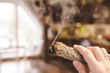 Woman hand holding herb bundle of dried sage smudge stick smoking. It is believed to cleanse...