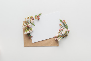top view of empty blank with brown envelope and flowers on grey background