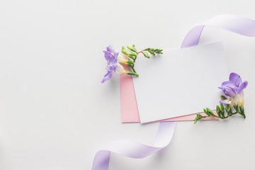top view of empty blank with pink envelope, purple flowers and silk ribbon on grey background