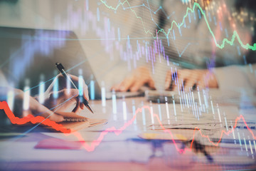 Close up of hands writing with double exposure of business charts. Financial concept.