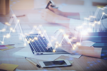 Hands typing on laptop. Business and Financial concept. Double exposure of stock market charts.