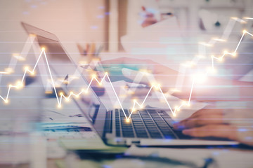 Hands typing on laptop. Business and Financial concept. Double exposure of stock market charts.