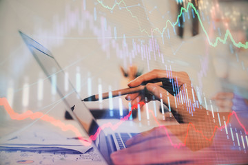 Hands typing on laptop. Business and Financial concept. Double exposure of stock market charts.