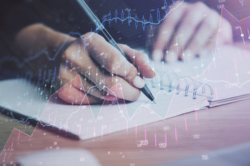 Close up of hands writing with double exposure of business charts. Financial concept.
