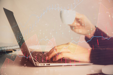 Hands typing on laptop. Business and Financial concept. Double exposure of stock market charts.