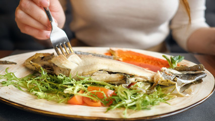 Close up of unrecognizable woman eating fish steak with knife and fork.