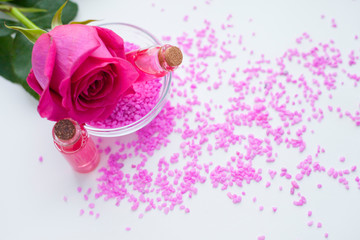 Aromatherapy. Small glass bottles with cosmetic oils. Sea salt. Fresh pink rose. Ingredients  for spa procedures on white background. Body care, skin care. Close up.