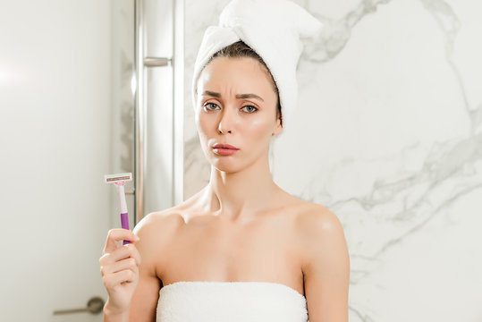 Young beautiful woman tired of shaving with razor blade wrapped in towels in the bathroom.  beauty makeup and skin care concept