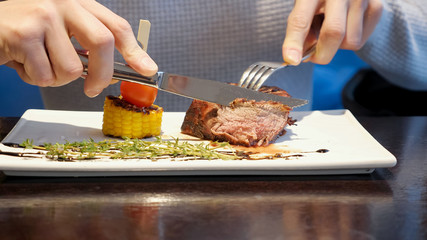 man cuts off a piece of steak and eats in cafe, close up