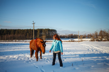 Red-haired girl goes with a horse in a snowy field
