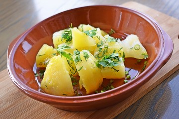 Delicious potatoes with butter and herbs in a clay dish on a wooden background.
