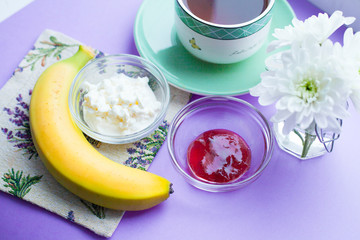 Healthy food concept. Muesli, fruits, curd and jam for productive day on the purple background. Top view. Space for a text.