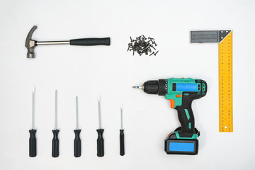 arranged drill with screwdrivers and hammer with pile of nails on white background, top view