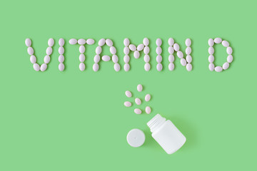 Pills dropped in shape of words vitamin D from bottle on green background. Flat lay, top view. Health care and medical concept.