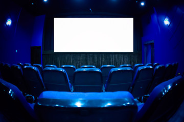 Empty cinema auditorium with empty white screen. Empty rows of theater or movie seats. Blue toned.