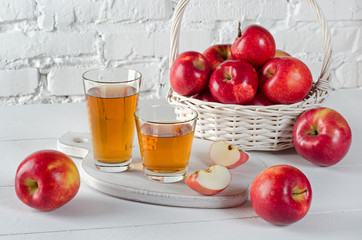 Apples and juice in glasses on  white table.