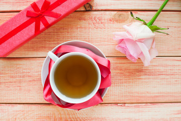 Cup of tea with pink rose and box on the wooden background. Holiday and date concept.Top view. Copy space. Close up.