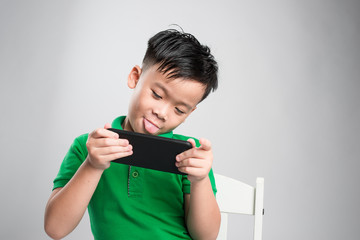 Portrait of an amused cute little kid playing games on smartphone isolated over gray background