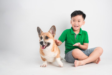 Portrait of a joyful little boy having fun with welsh corgi dog on the floor at studio.