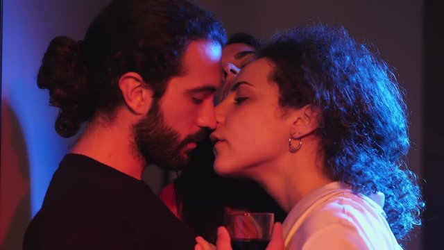 Sensual kiss among two women and man in night club.Polygamy, polyamory