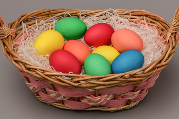Obraz na płótnie Canvas Easter colored eggs lie in a wicker basket on a gray background. Easter. Horizontal photography.