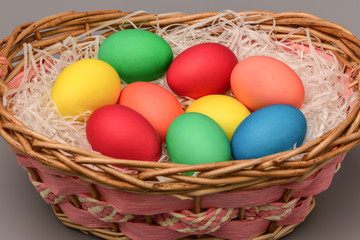 Easter colored eggs lie in a wicker basket on a gray background. Easter. Horizontal photography.