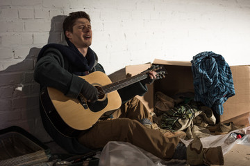 homeless man playing guitar and singing while sitting un rubbish dump