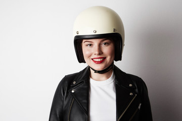 Handsome woman wearing black leather jacket and white moto helmet over background. Fashion, glamour and moto wear concept