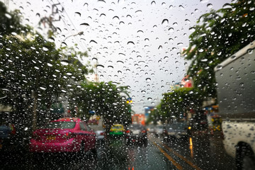 Road view through front car window mirror with rain drops.