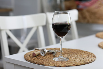a glass of wine and some wine tools on a white wooden surface. Red wine