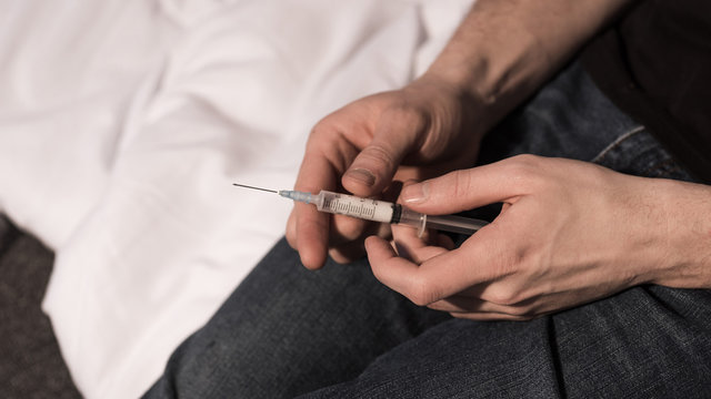 selective focus of narcomaniac man holding syringe with dose of heroin