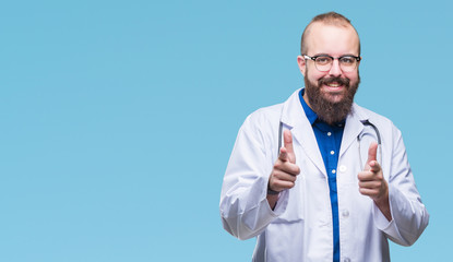 Young caucasian doctor man wearing medical white coat over isolated background pointing fingers to camera with happy and funny face. Good energy and vibes.