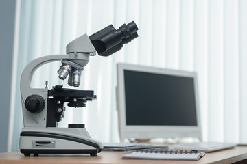 Microscope and a computer on a table in a laboratory on a window light background.