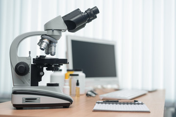 Fototapeta na wymiar Laboratory table with microscope, flasks and a desktop computer above on a window light background. Medicine, pharmacology, pharmacy abstract background.