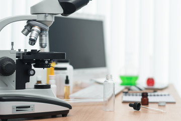 Laboratory table with microscope, flasks and a desktop computer above on a window light background. Medicine, pharmacology, pharmacy abstract background.