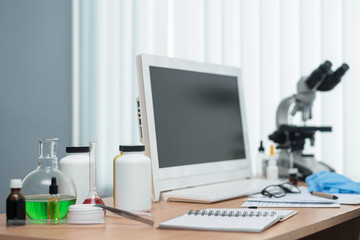 Laboratory table with microscope, flasks and a desktop computer above on a window light background. Medicine, pharmacology, pharmacy abstract background.