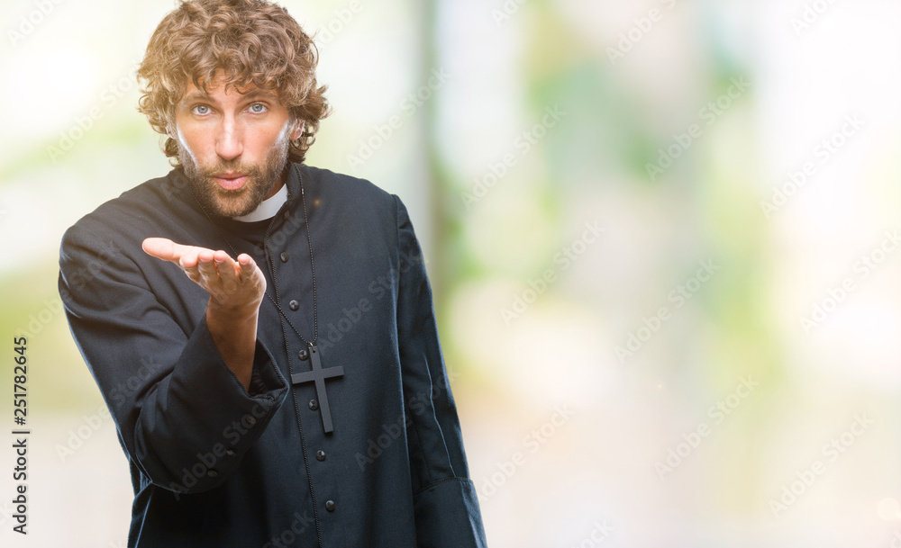 Wall mural Handsome hispanic catholic priest man over isolated background looking at the camera blowing a kiss with hand on air being lovely and sexy. Love expression.