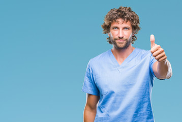 Handsome hispanic surgeon doctor man over isolated background doing happy thumbs up gesture with hand. Approving expression looking at the camera with showing success.