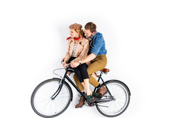 Smiling stylish couple riding bicycle together on white background