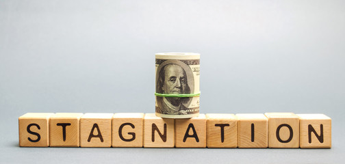 Wooden blocks with the word Stagnation and dollars. Prolonged period of slow economic growth,...