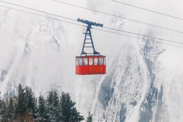 Naadloos Fotobehang Airtex Rode skilift op de achtergrond van de winterbergen. De rode aanhangwagen van de oude kabelbaan gaat naar de bergtop van het skigebied. Retro gondel. © Т Т