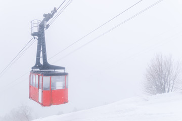 Red Ski lift in the background of the winter mountains. The red trailer of the old cable car moves to the mountain top of the ski resort. Retro gondola.