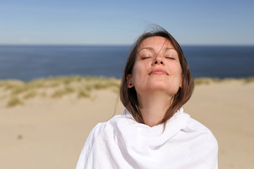 Beautiful dark hair young white european woman wrapped in white cloth with eyes closed. Close up. Shot on Parnidis dune in Nida, Lithuania, in Curonian Spit. Sunny day with blue sky.