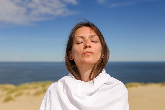 Beautiful dark hair young white european woman wrapped in white cloth with eyes closed. Close up. Shot on Parnidis dune in Nida, Lithuania, in Curonian Spit. Sunny day with blue sky.