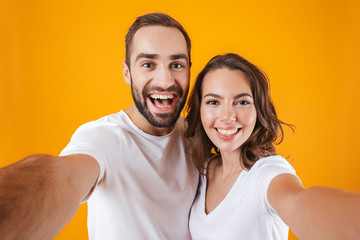 Fototapeta premium Portrait of two contented people man and woman smiling while taking selfie photo, isolated over yellow background