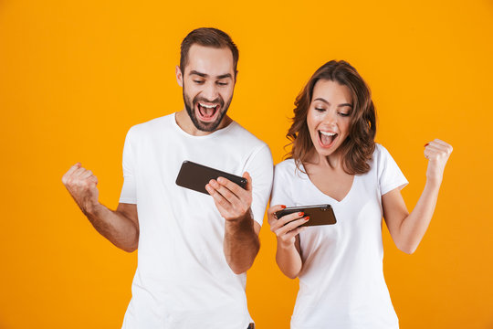 Image of happy man and woman playing together video games on smartphones, isolated over yellow background