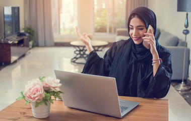 Pretty young middle eastern woman talking on mobile phone and using laptop at home